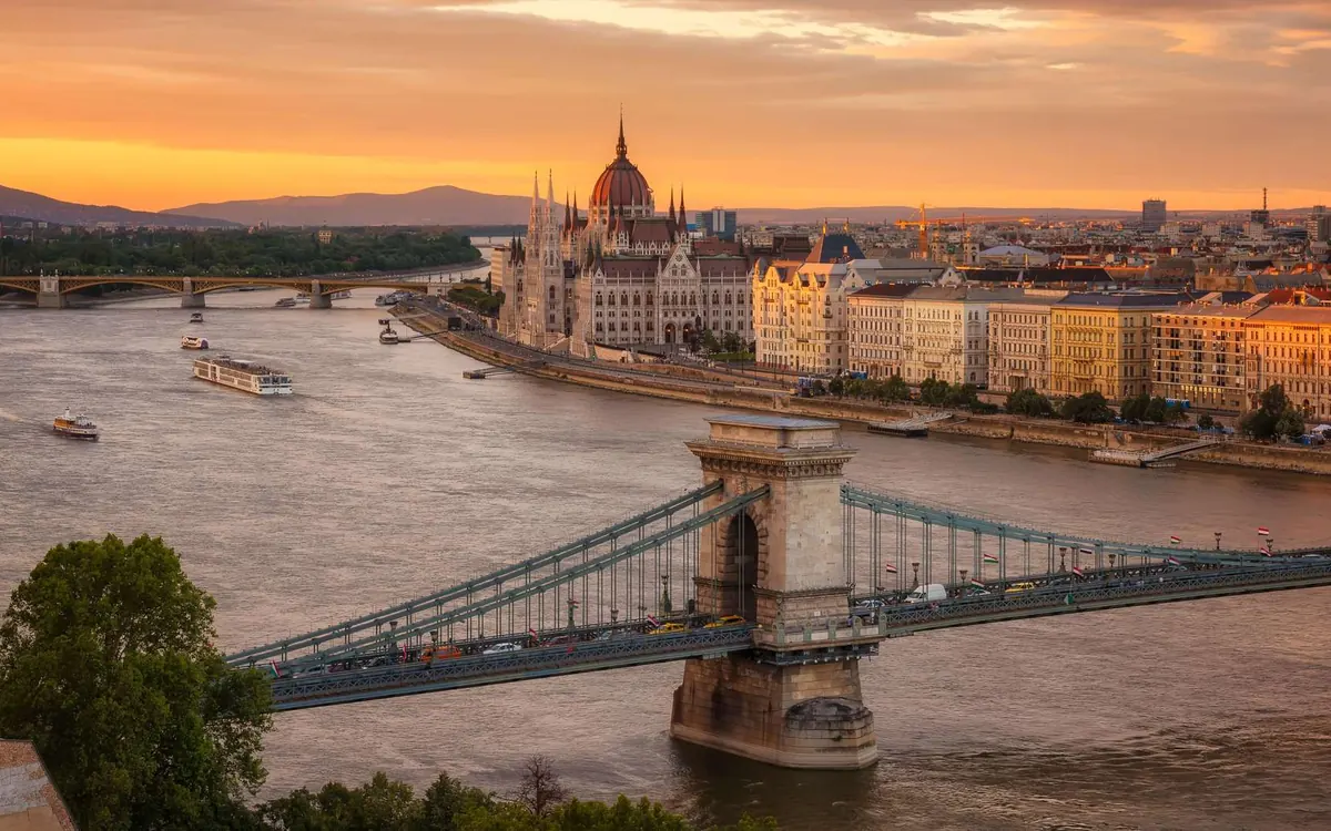 The Parliament building on the river in Budapest at sunset, with the Chain Bridge in front