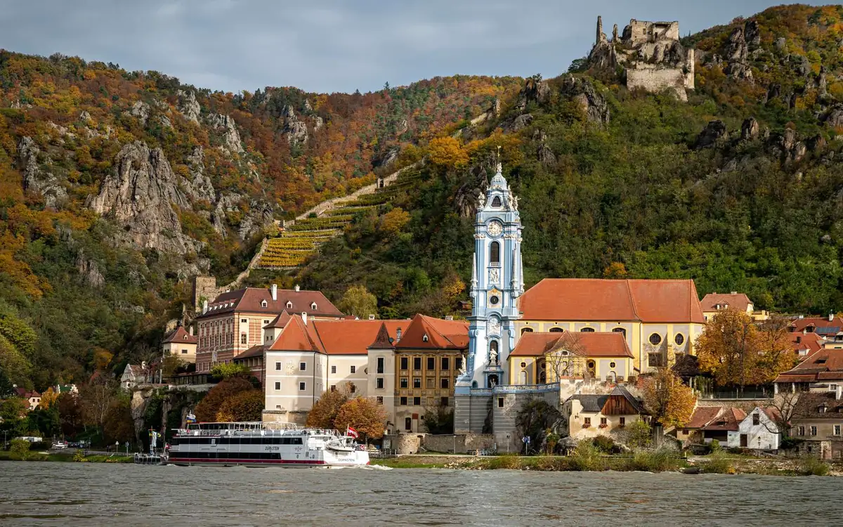 A white riverboat moored below a blue and white church tower, a ruined castle on the hill above