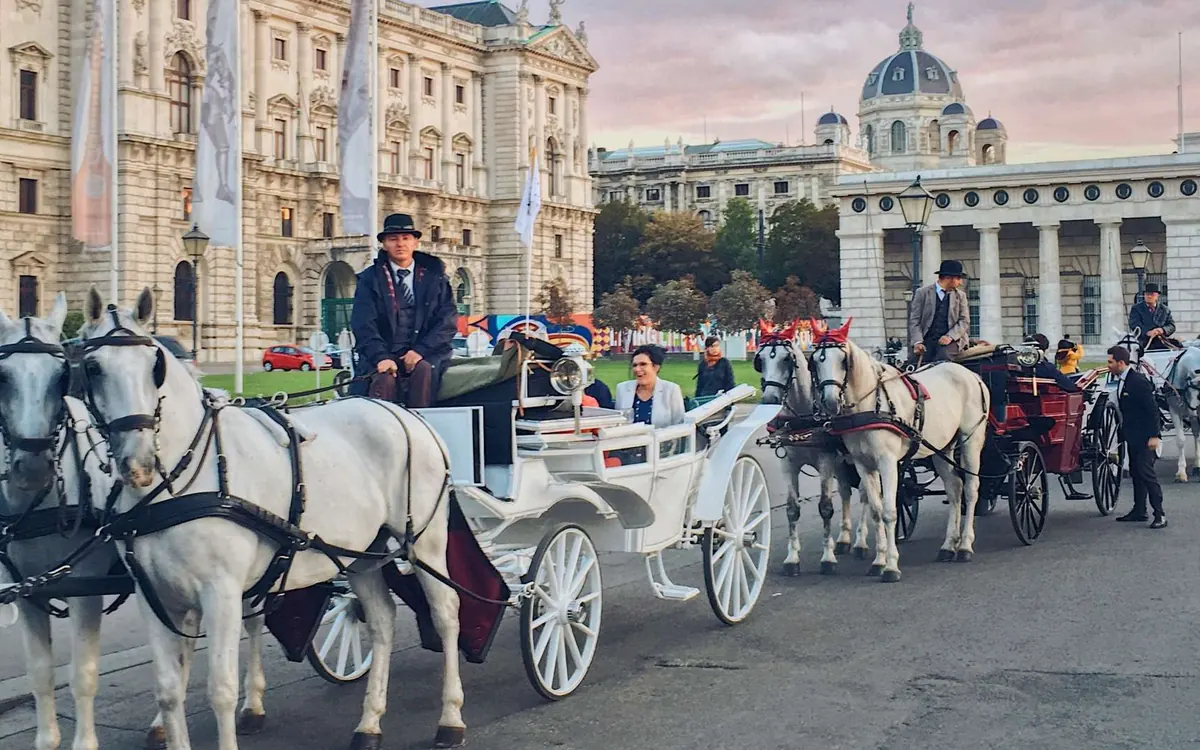Horse-drawn fiakers with white horses and coachmen in hats waiting on a square