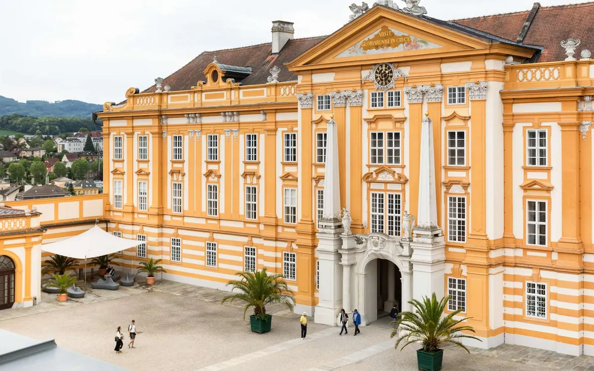 The yellow and white baroque courtyard of Melk Abbey, potted palms and a few visitors