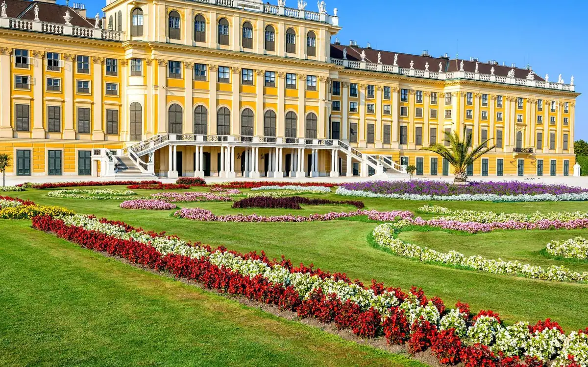 The yellow façade of Schönbrunn Palace behind flower beds of red, white and purple blooms