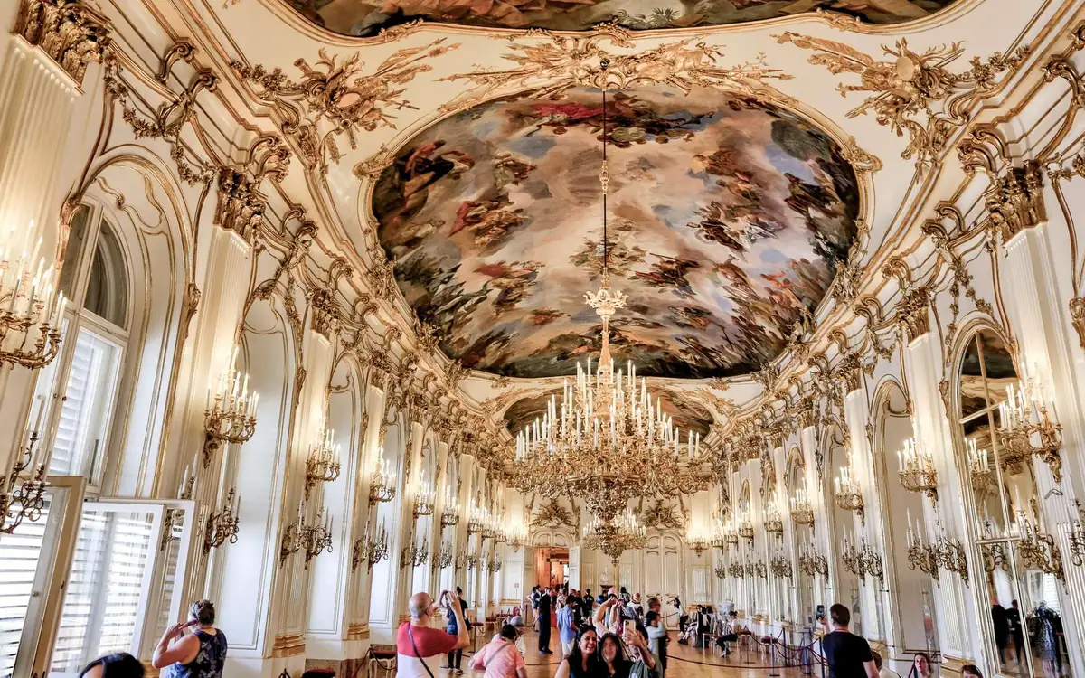 A long white-and-gold hall inside Schönbrunn Palace with a painted ceiling and chandeliers