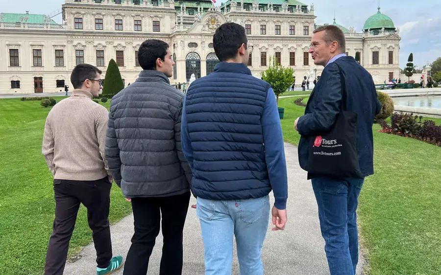 A guide and three visitors on a garden path facing the Belvedere