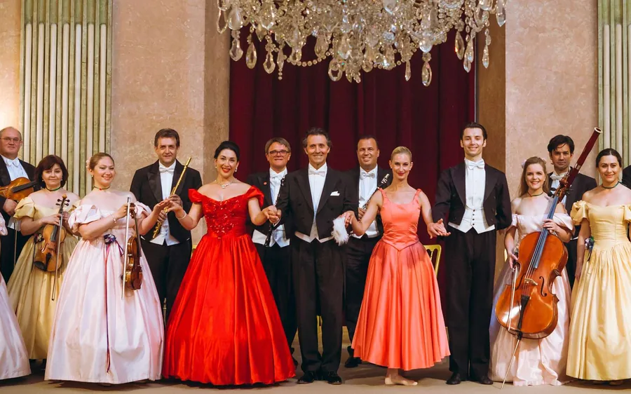 Musicians and dancers in ball gowns posing under a chandelier