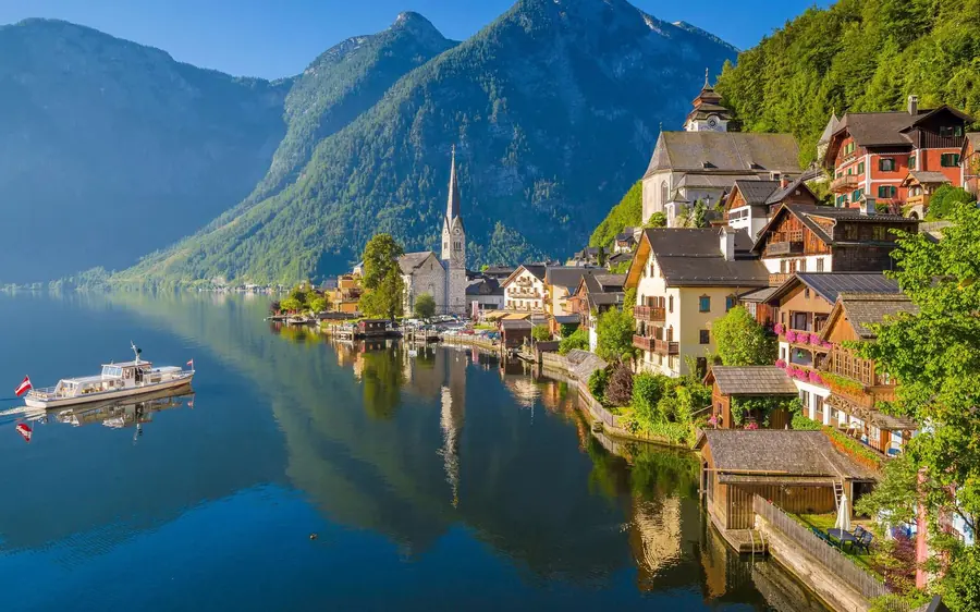 Hallstatt and a passing boat reflected in the lake below green peaks