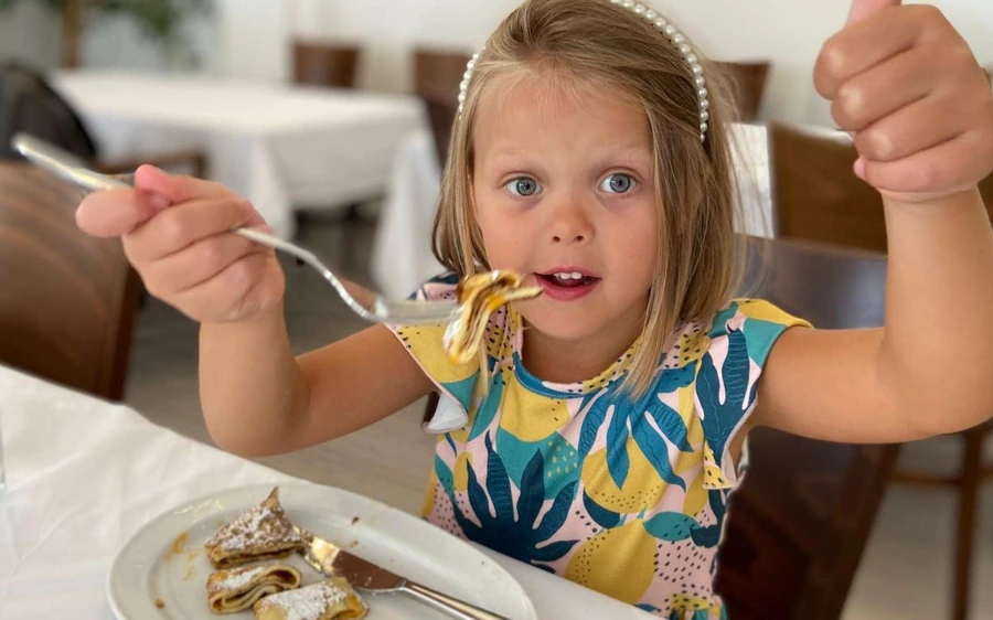A young girl lifting a forkful of strudel at a dining table
