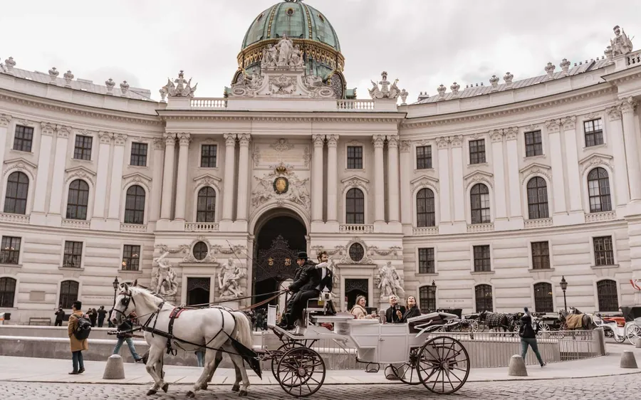 A white horse-drawn carriage in front of the domed Hofburg gate