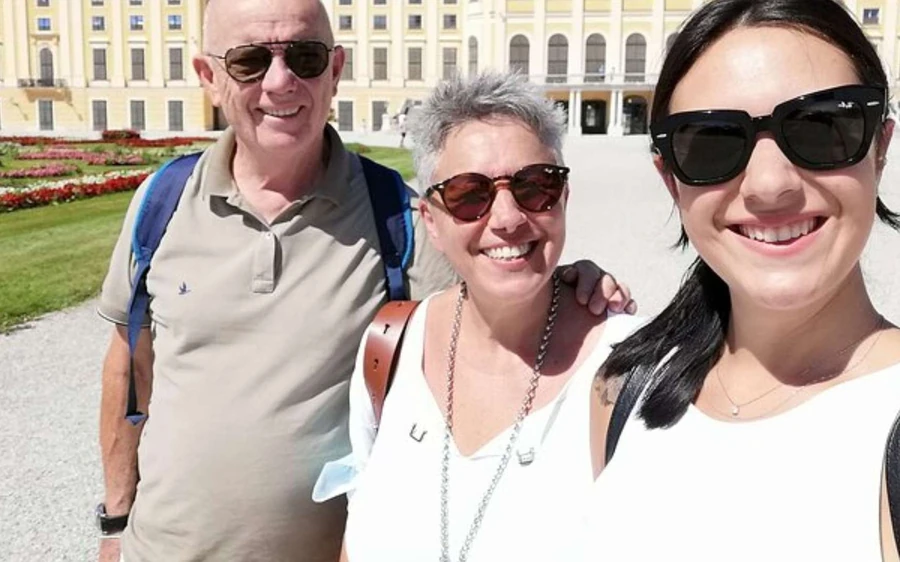 Three smiling visitors taking a selfie in front of a palace garden