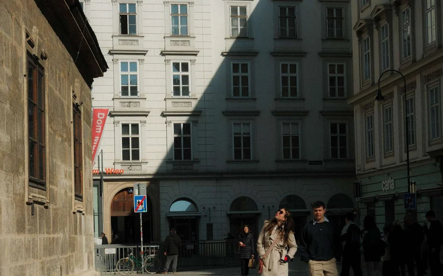 People walking along a shaded street between tall old buildings