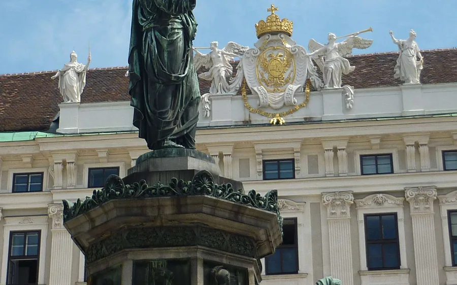 A statue in front of the crowned imperial crest on the Hofburg