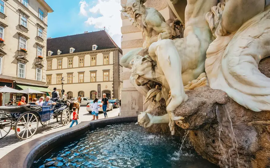 A marble fountain with sculpted figures beside a fiaker on an old-town street