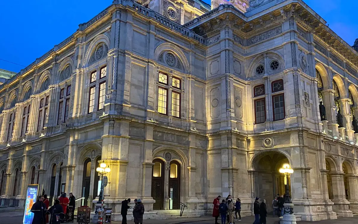 The Vienna State Opera house lit up at dusk with people on the pavement